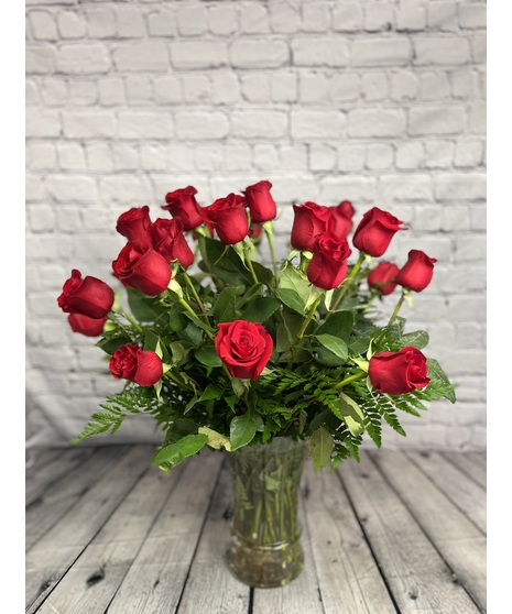 One dozen red roses and greenery in a clear glass vase.
