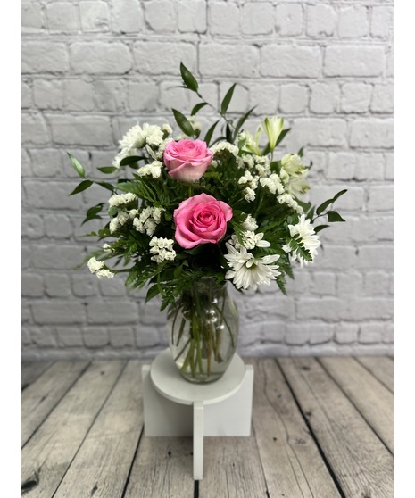 White daisies, pink roses and other assorted flowers in a clear glass vase.