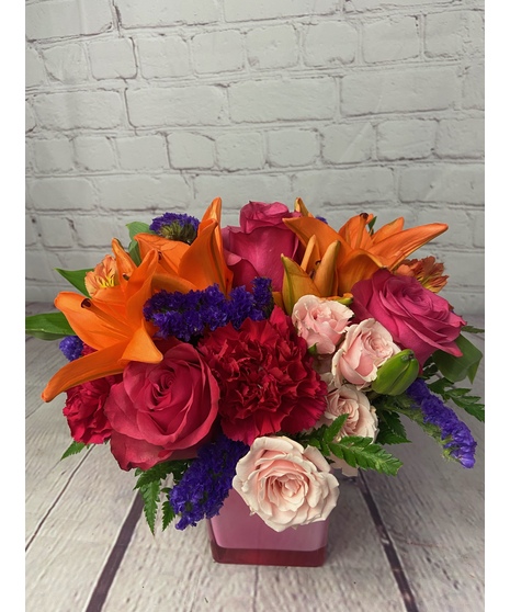 Pink and peach colored roses, asiatic lilies,  alstroemeria and carnations in a pink cube vase.