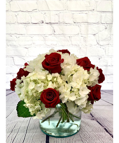 Red roses and white hydrangea in a clear glass cylinder vase.