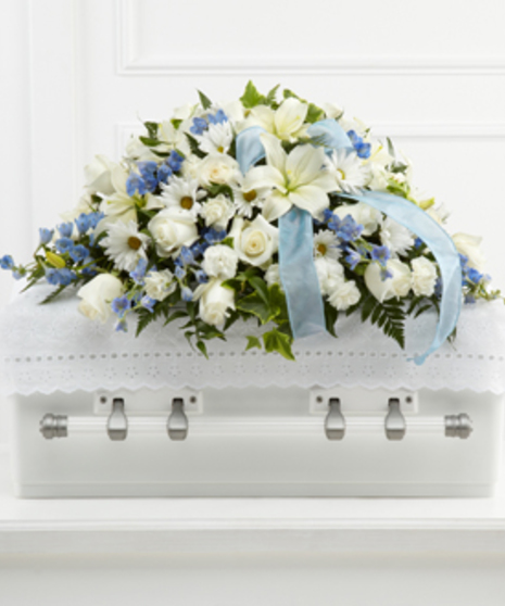 Casket spray of white roses, daisies, and more with blue delphinium and blue ribbon. 