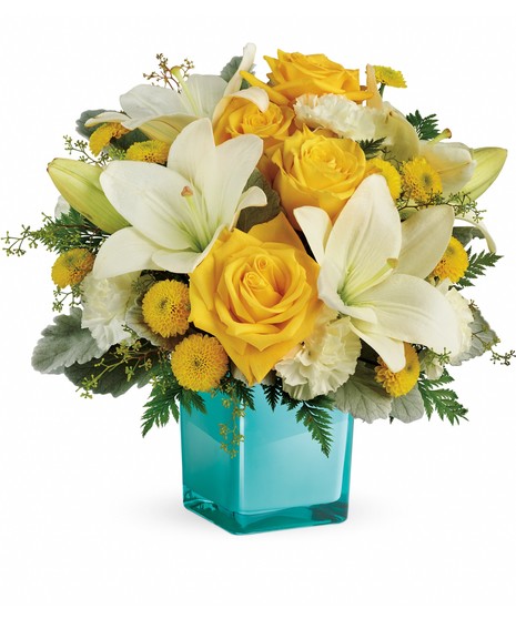 Yellow and white flowers in a teal glass cube vase.